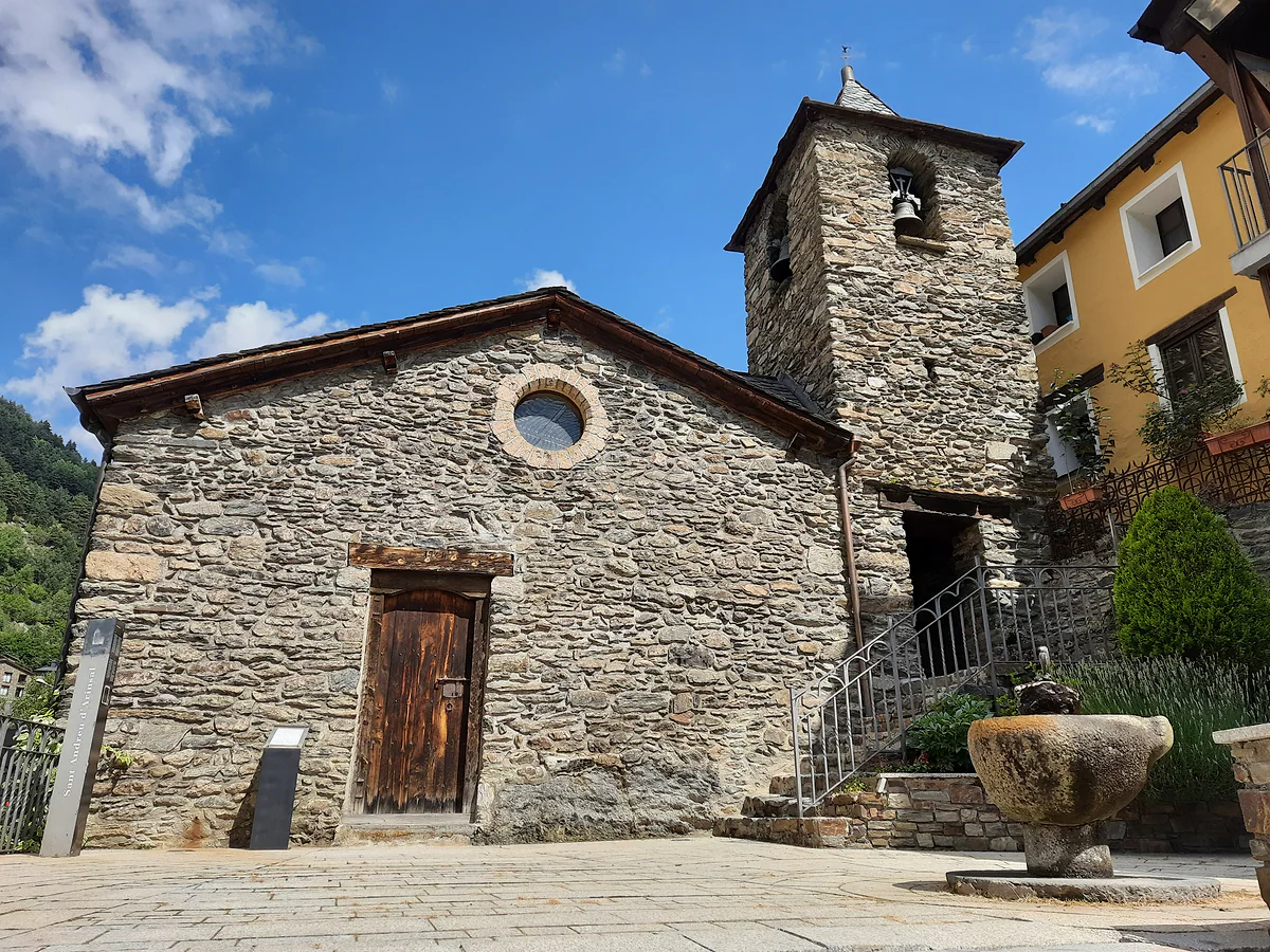 La iglesia de Sant Andreu d'Arinsal, de piedra, con campanario cuadrado y fuente delante