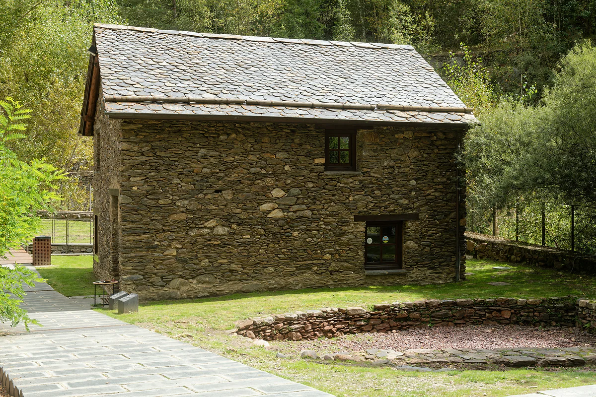 Edificio de piedra y pizarra de la Farga Rossell, antigua forja de hierro de La Massana, entre árboles