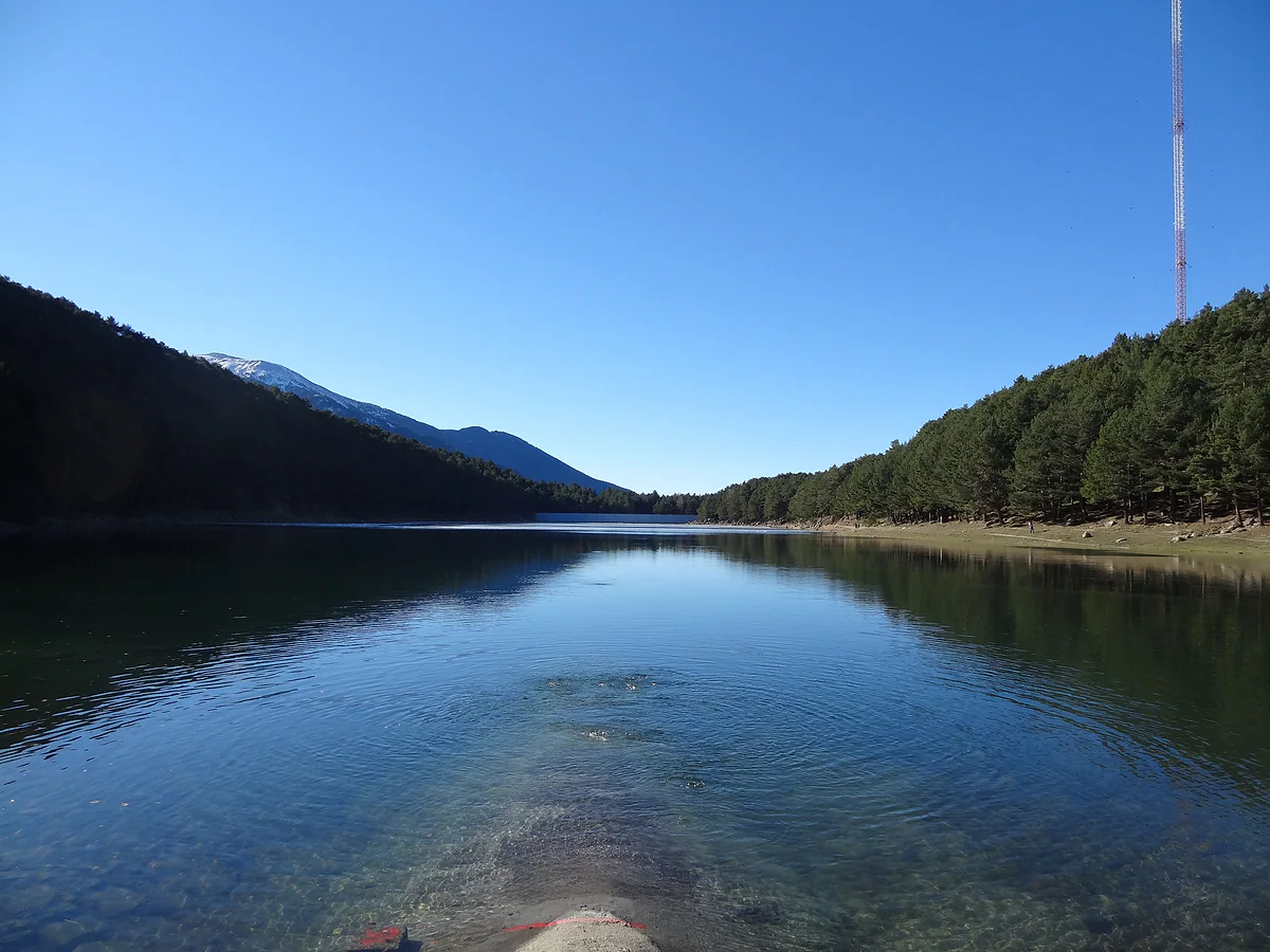 El lago de Engolasters en un día despejado, con agua transparente y laderas de pinos a ambos lados