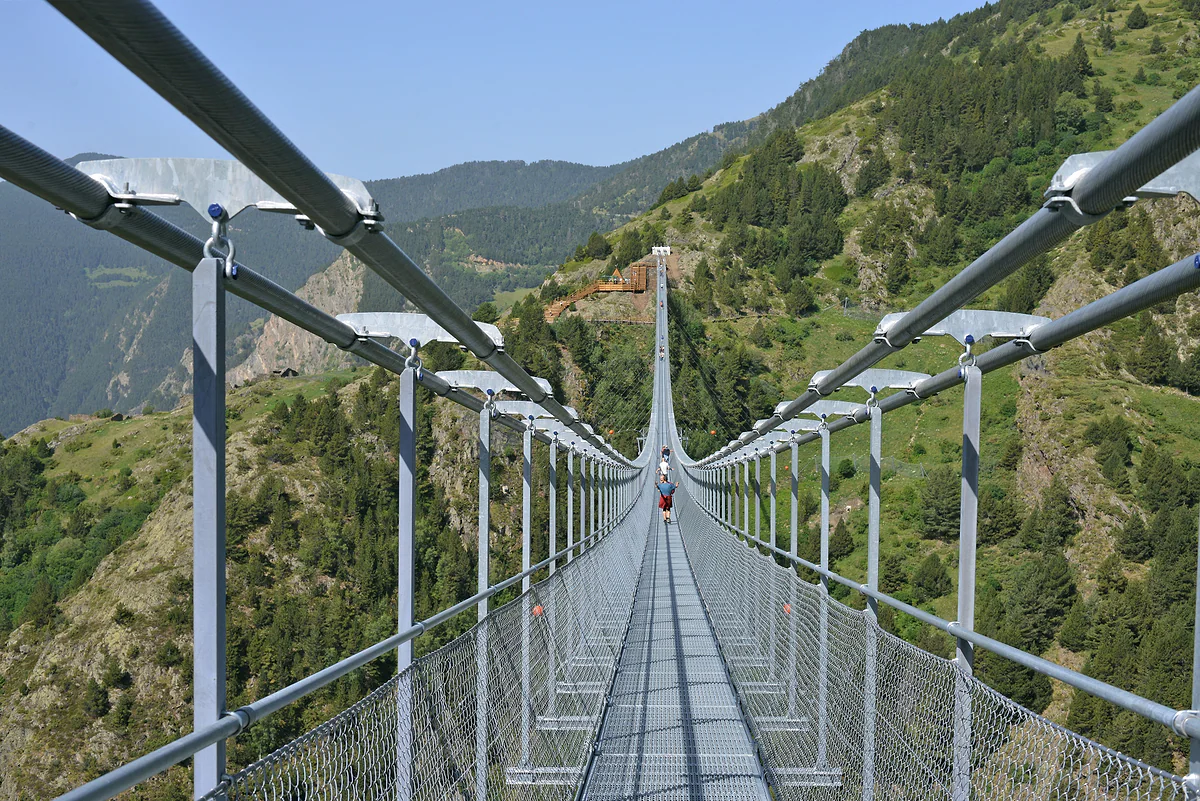 La pasarela del puente tibetano de Canillo vista desde la entrada, con barandillas y montañas verdes