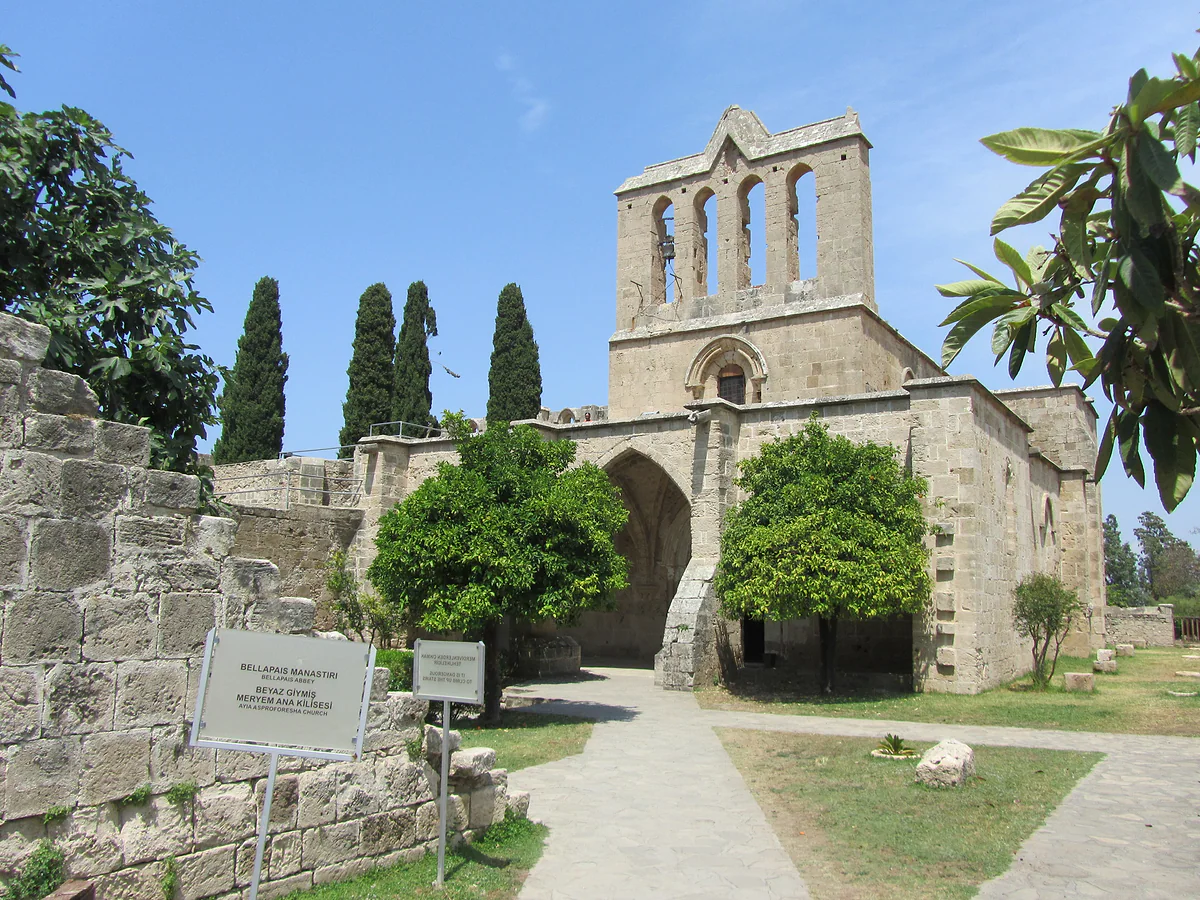 The church of Bellapais Abbey with its arched belfry, among cypresses and orange trees, above Bellapais village
