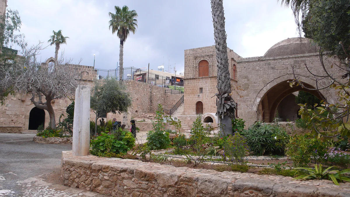 The courtyard of Ayia Napa monastery, with its garden, palm trees, golden stone walls and the fountain dome behind, in the centre of town