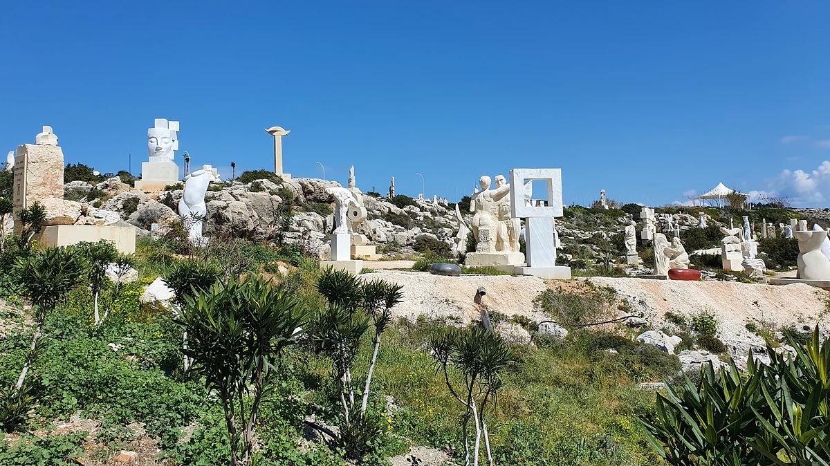 White stone sculptures scattered among rocks, dragon trees and scrub in the Ayia Napa sculpture park, under a clear blue sky