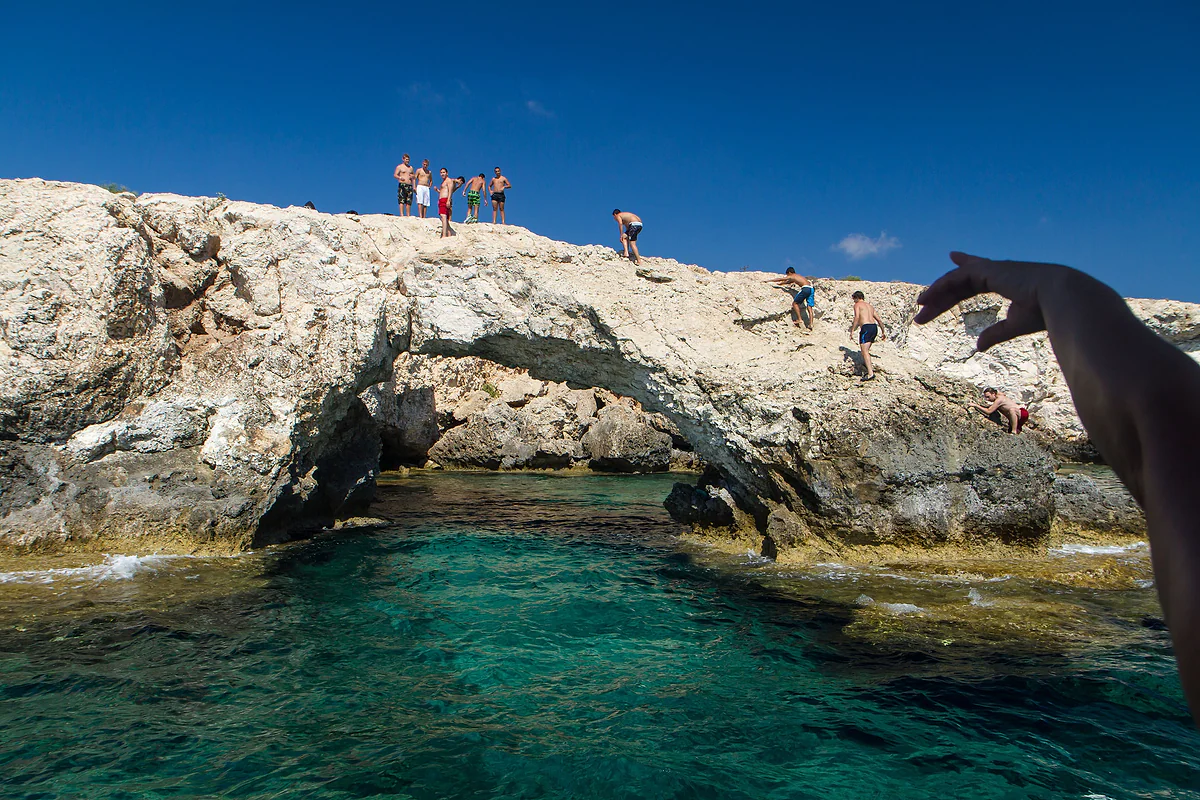 The Love Bridge at Ayia Napa, a natural rock arch over turquoise water, with people standing on top and others on the rocks