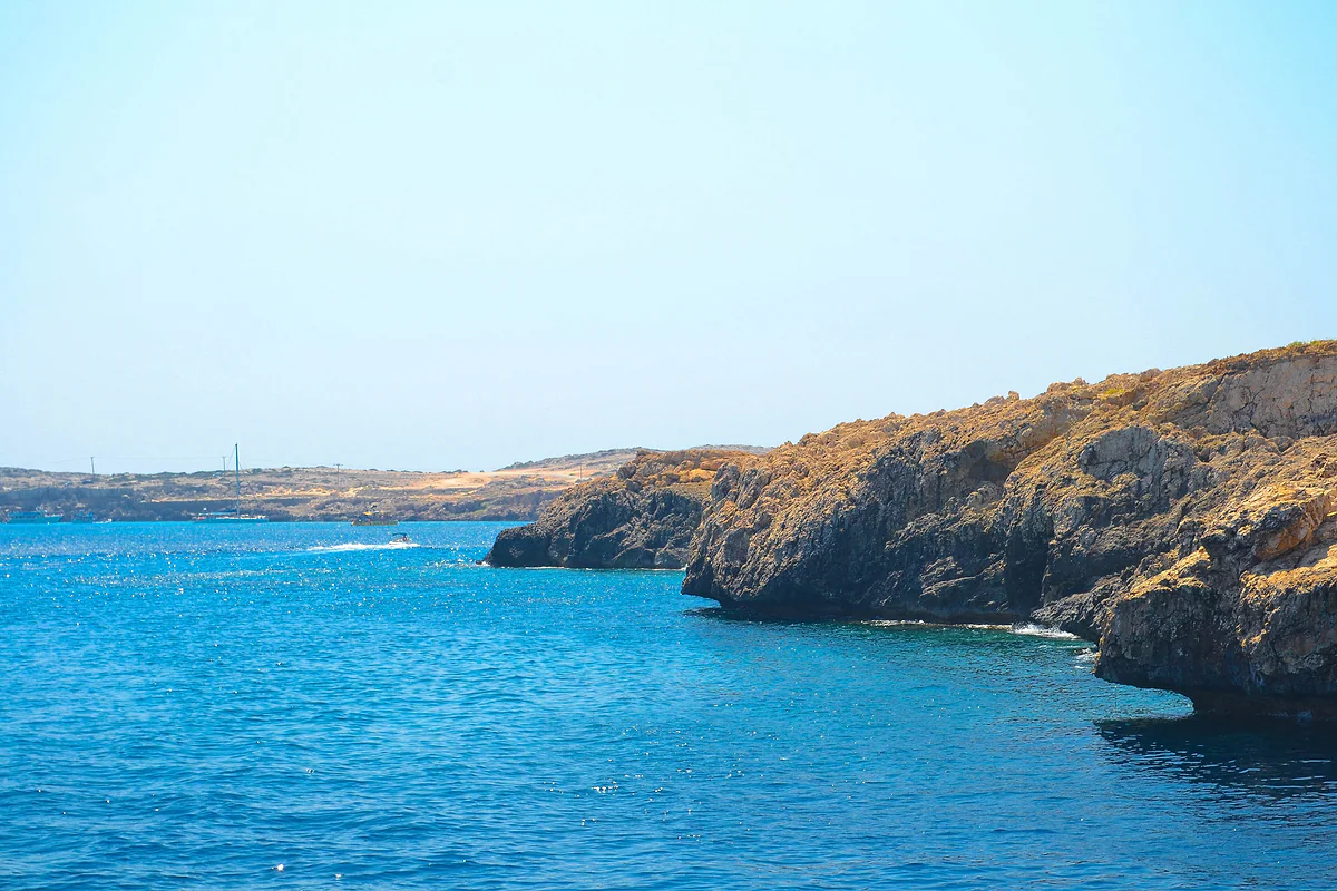 The golden limestone cliffs of Cape Greco dropping into turquoise and blue sea, with the Ayia Napa coast in the distance