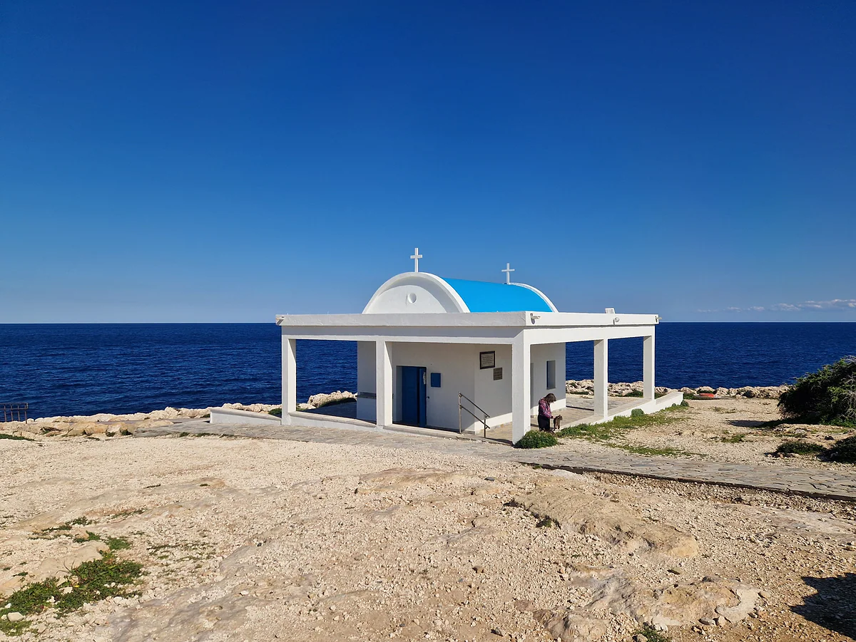 The white, blue-domed chapel of Agioi Anargyroi at Cape Greco, on a rocky platform facing the deep blue sea of eastern Cyprus
