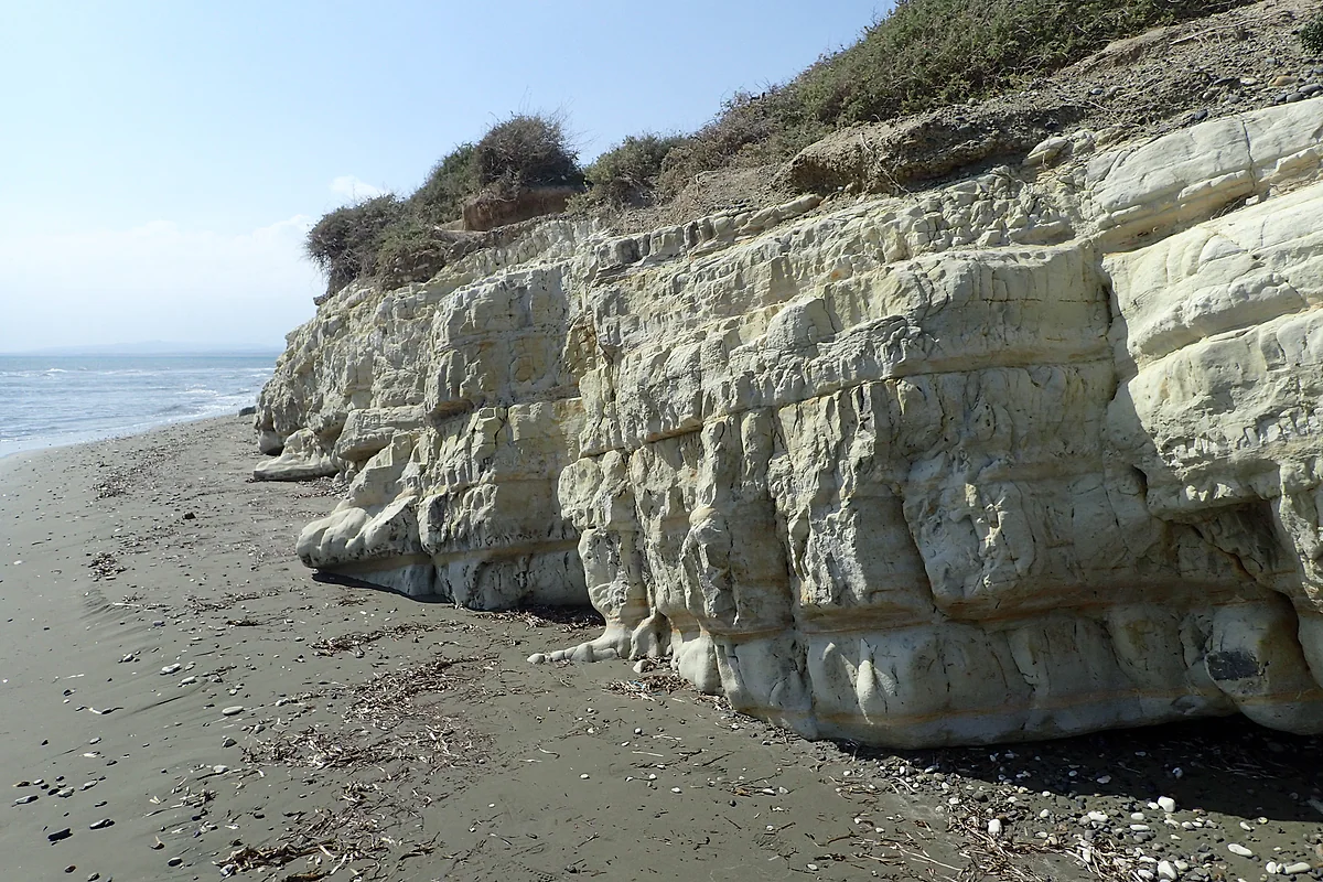 Weathered white rocks on the shore at Cape Kiti, with the dark sandy beach and the sea running alongside