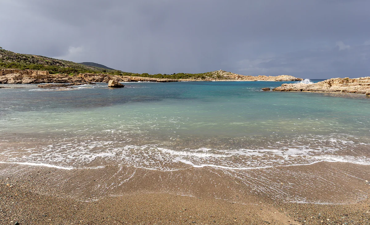 A sandy cove on the Akamas peninsula with clear water and low rocks on either side, on the west coast of Paphos district
