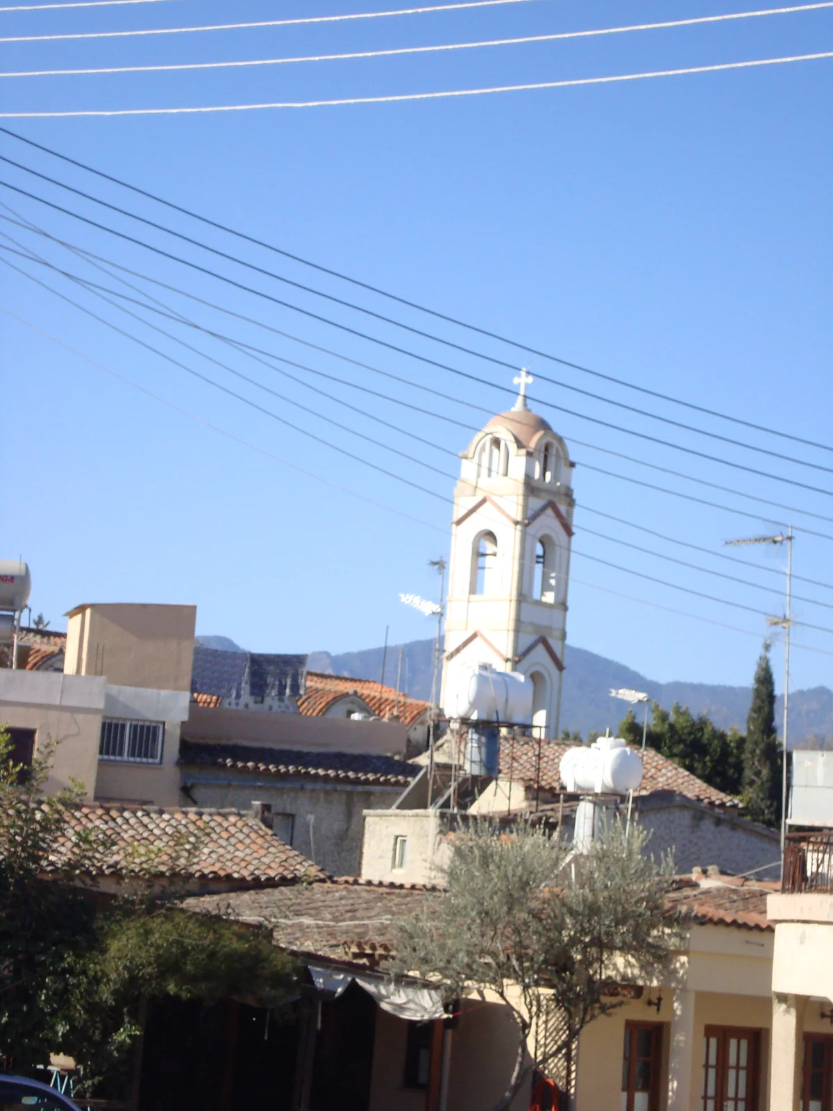 The white bell tower of the church in Lythrodontas rising above the village rooftops, with mountains behind