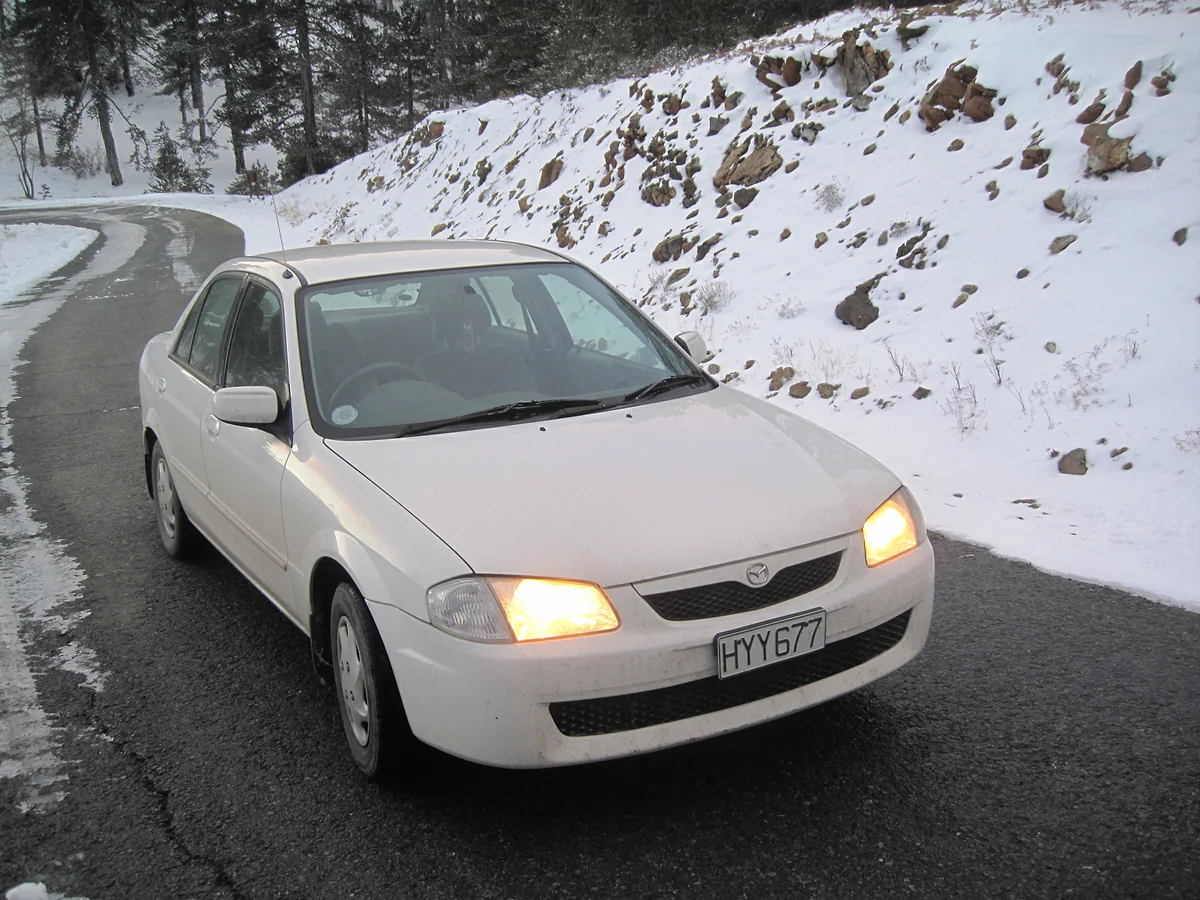A car on the road climbing Mount Olympus in winter, with a snowy bank and Troodos pine trees behind it