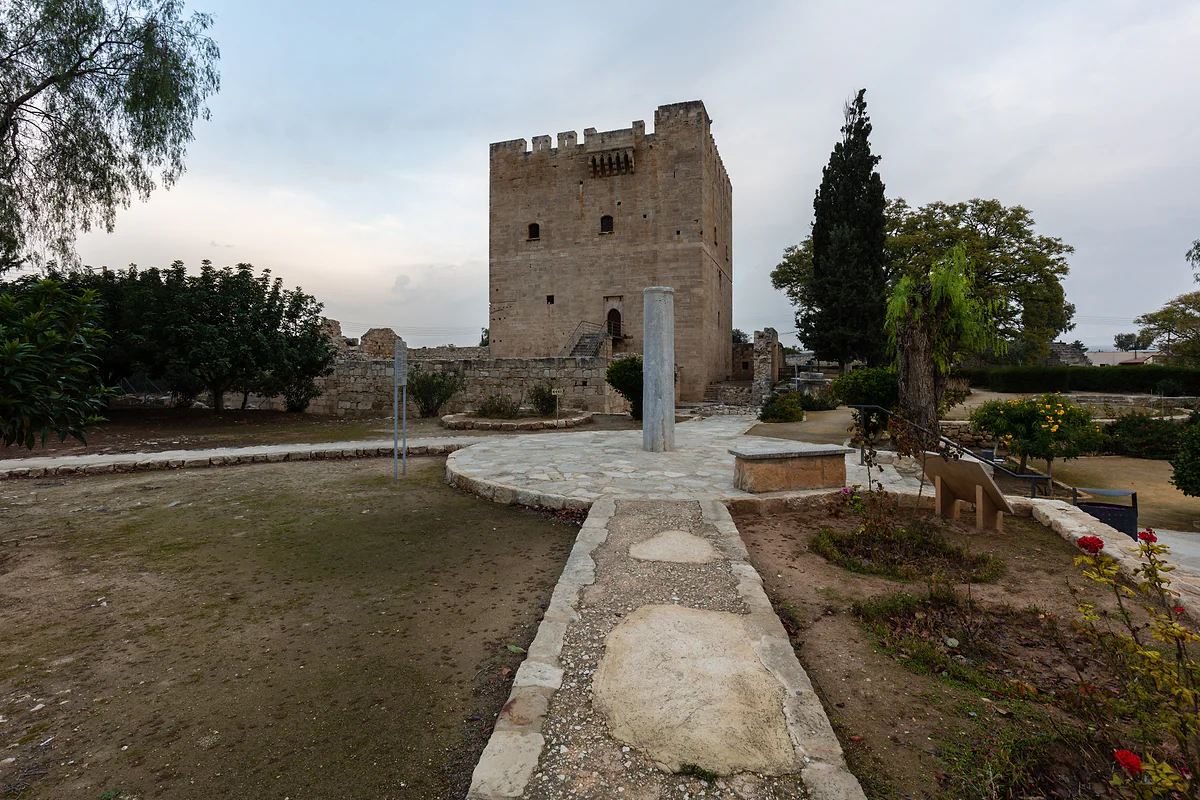 Kolossi Castle seen from the garden, with the keep behind, cypress trees and a stone path leading towards it