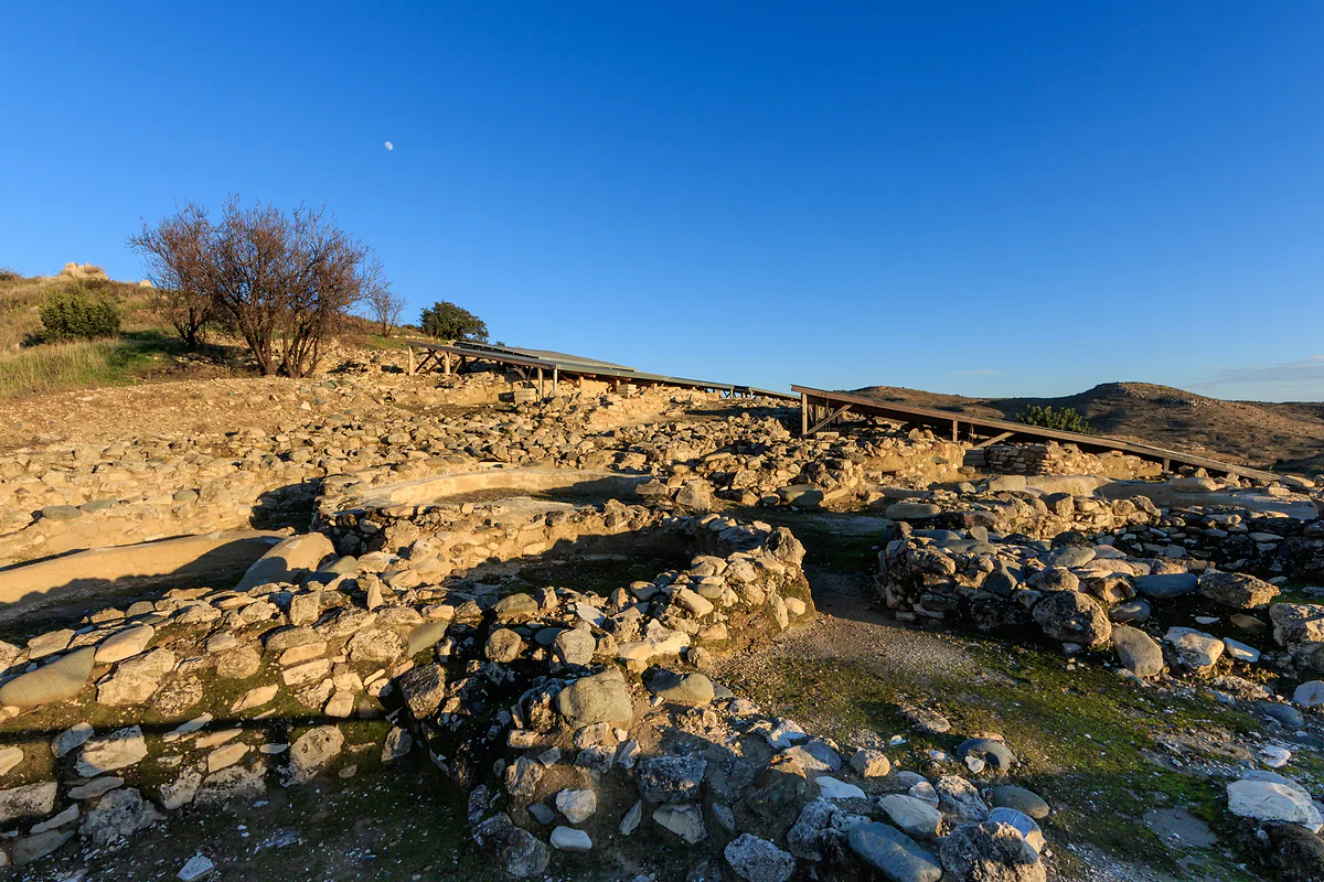 The round stone walls of the Neolithic settlement of Choirokoitia on the hillside, with the walkway and blue sky