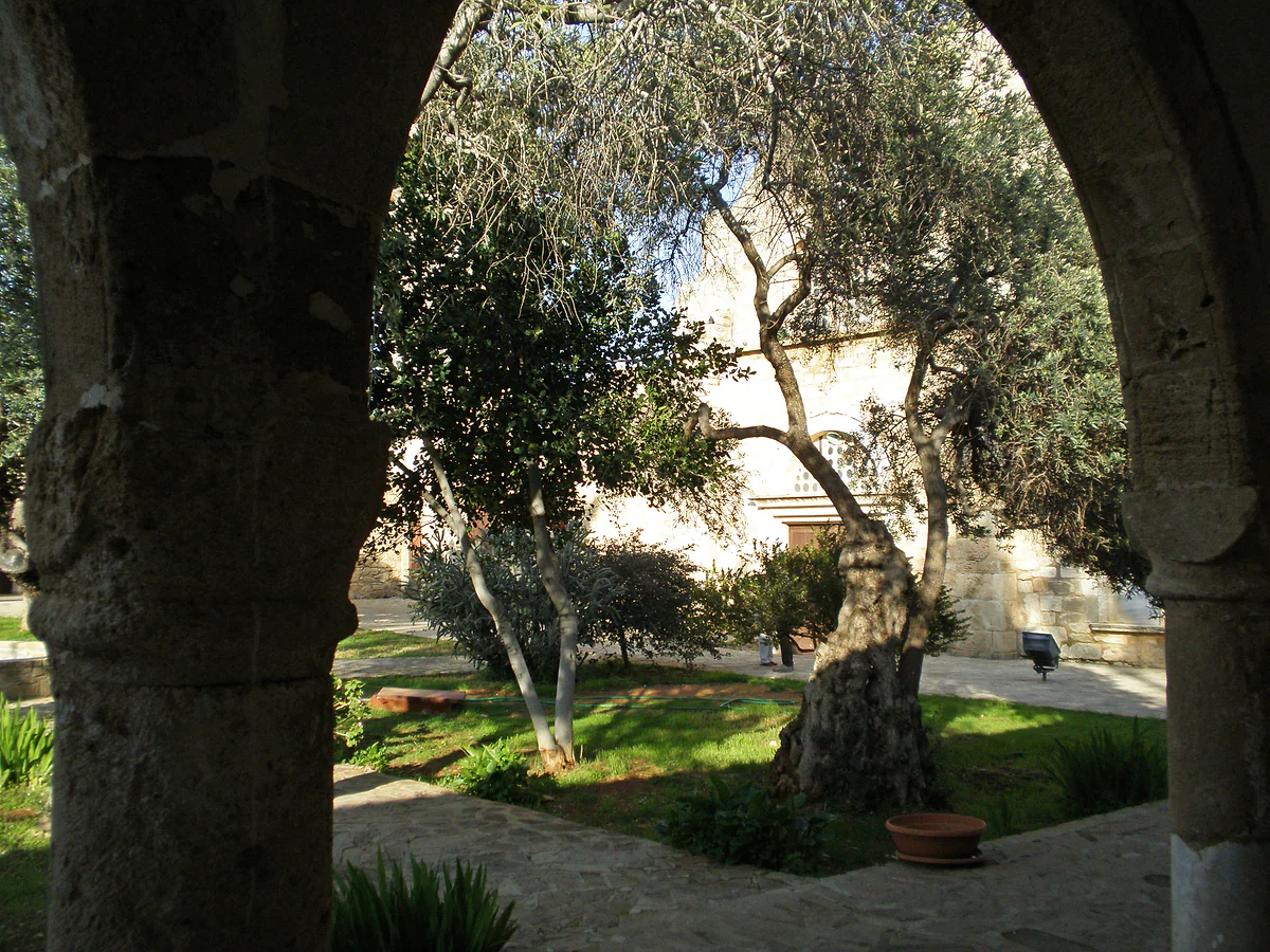 The garden of St Barnabas Monastery seen through the cloister arches, with olive trees and the stone church behind