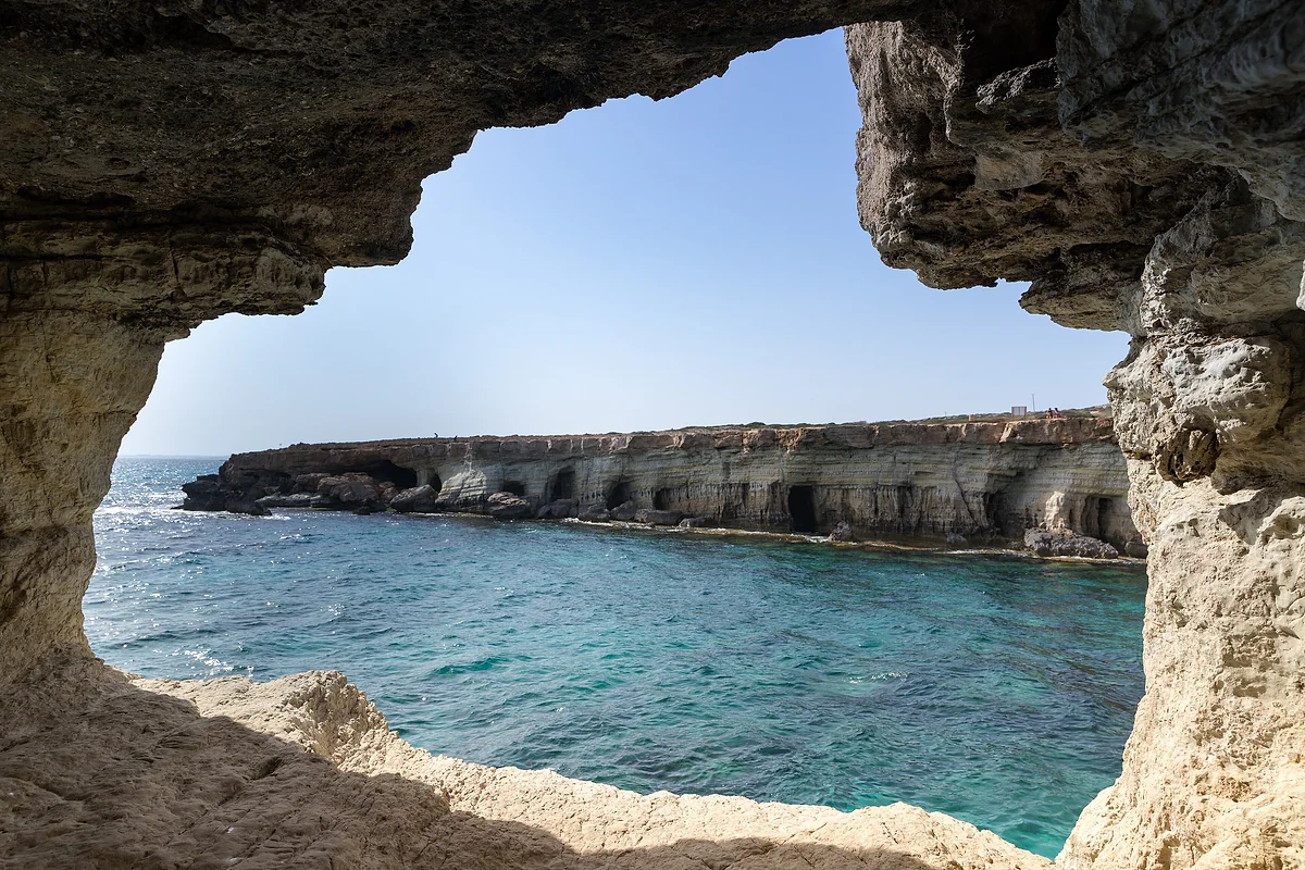 The Ayia Napa sea caves coast seen through the mouth of a grotto, with honeycombed cliffs and turquoise water below them
