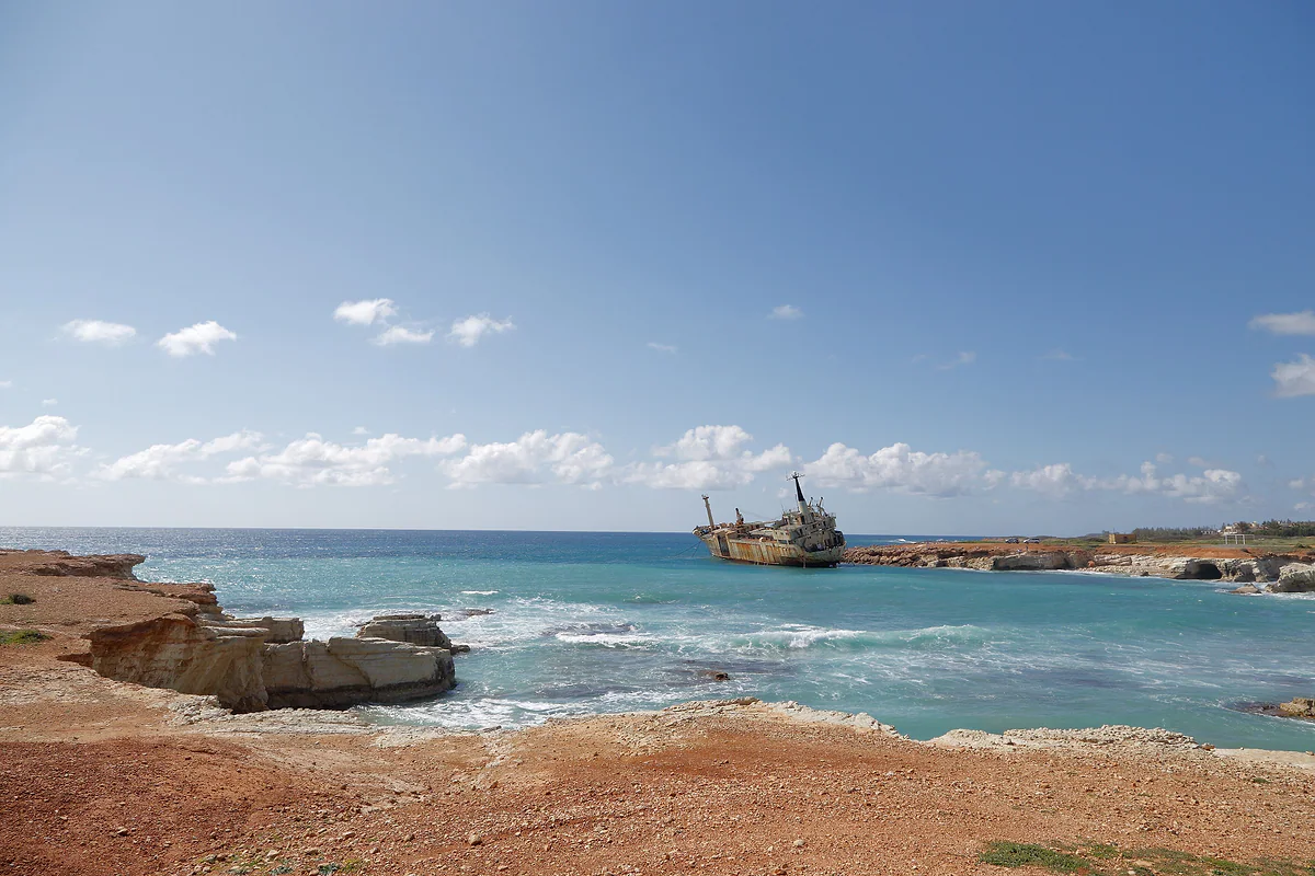 The rocky coast of the Pegeia sea caves, with turquoise water and the stranded Edro III in the distance, by the Akamas peninsula