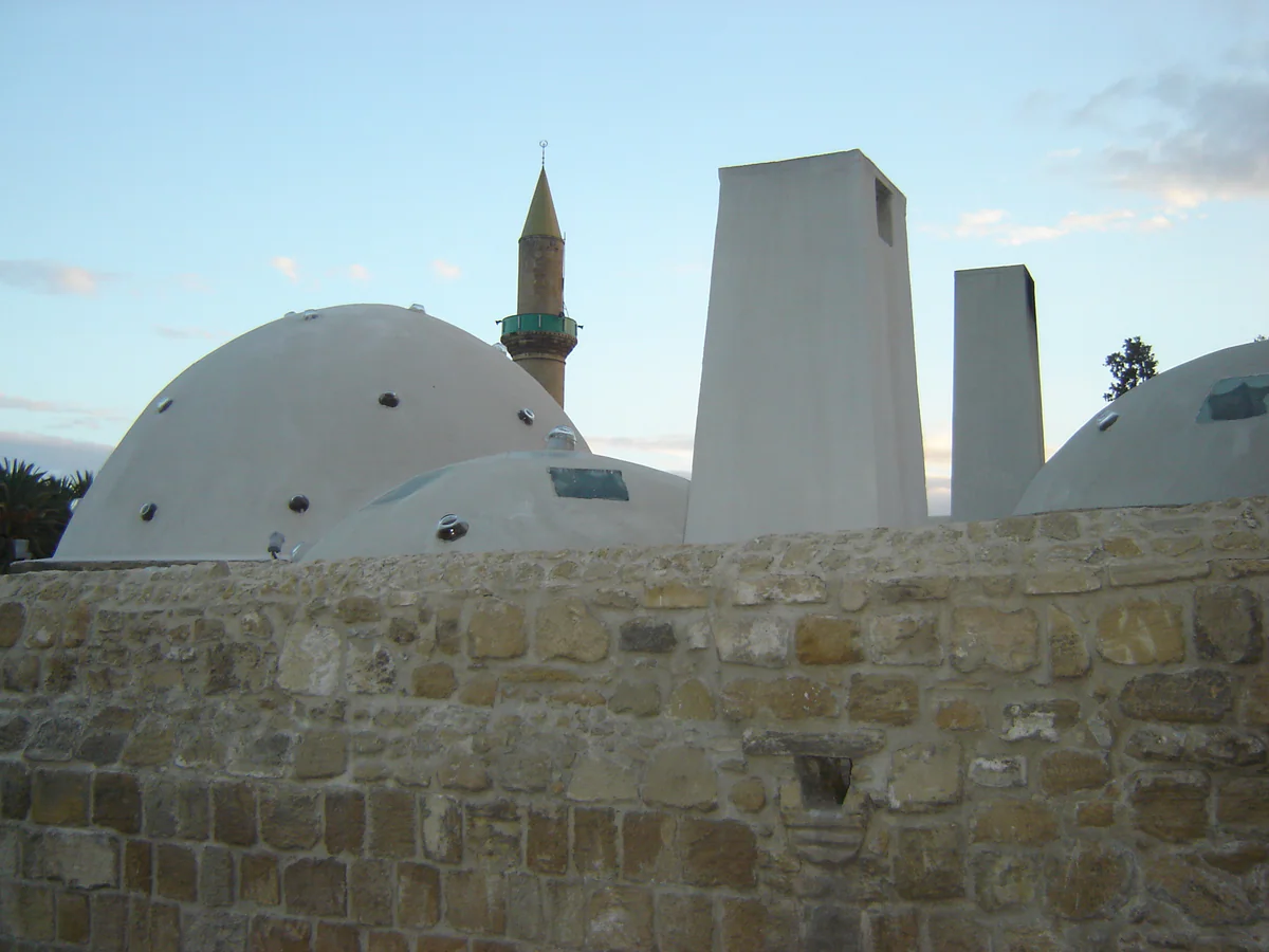 The white domes of the Omerye hammam in Nicosia behind a stone wall, with the minaret of the mosque rising behind