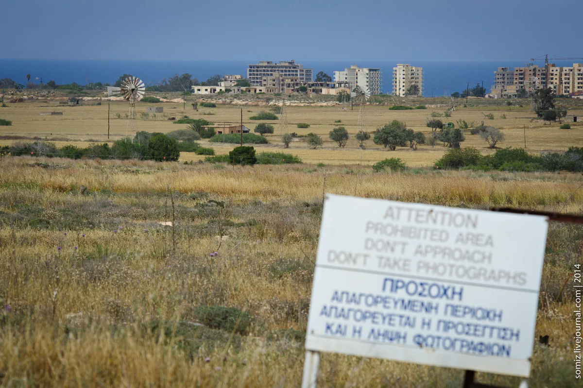 Dry fields at Deryneia with a prohibited area sign and, in the distance, the tall buildings of Varosha beside the sea