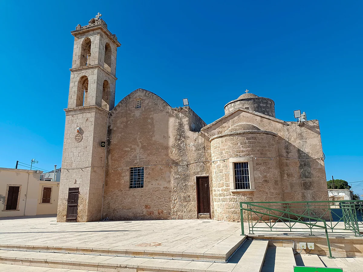 The church of the Panagia in Deryneia, built of golden stone with a dome and a tall bell tower, beside a square with steps