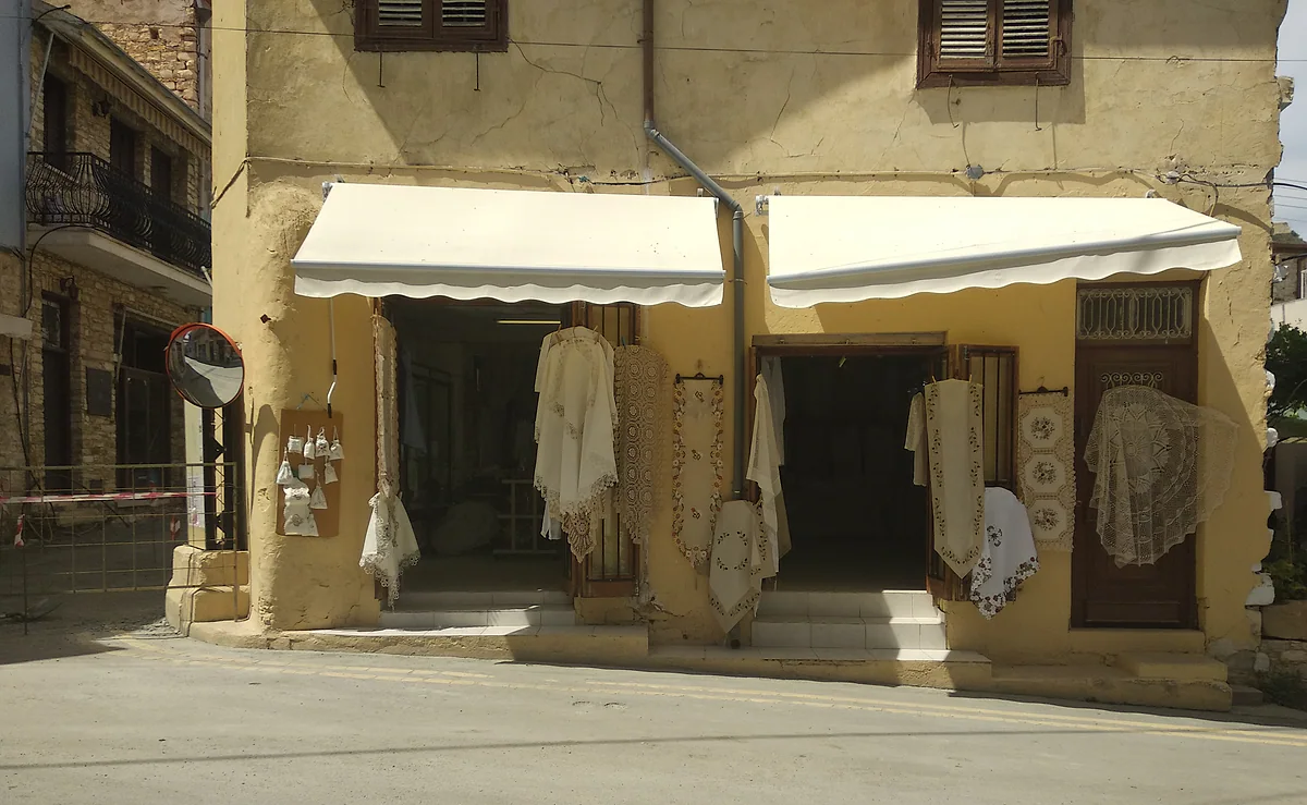 A lace shop in Lefkara, with white tablecloths and blouses hanging at the entrance beneath two awnings