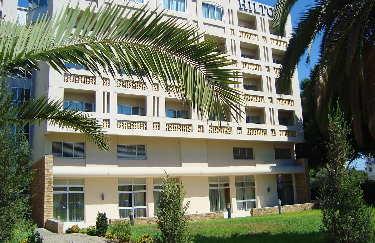 The facade of the Hilton hotel in Nicosia, a multi-storey building with balconies, framed by palms and lawn