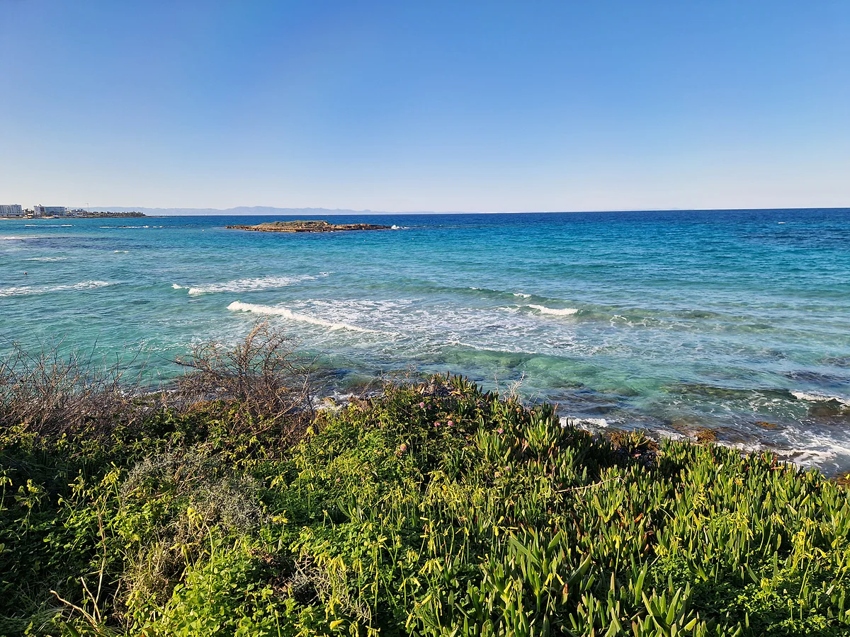 The coast at Protaras by Fig Tree Bay, with turquoise water and a rocky islet offshore, in Cyprus