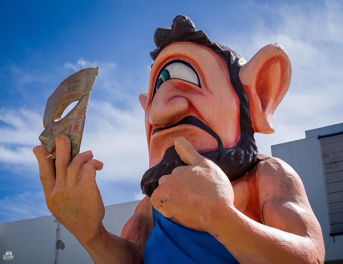 A giant papier-mache figure prepared for the Limassol Carnival parade, set against a bright blue sky