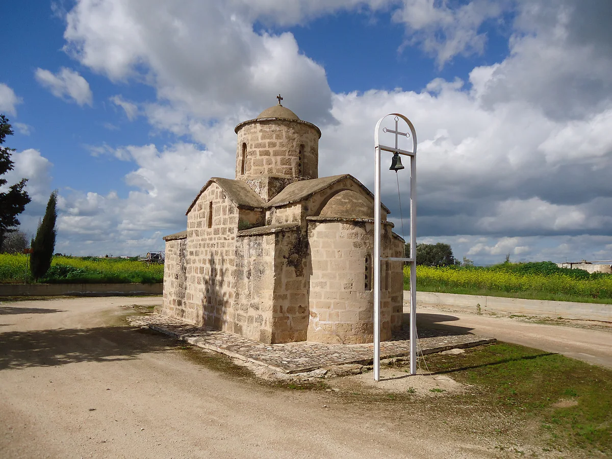 The small stone chapel of Agios Andronikos outside Frenaros, with its dome and a bell frame standing beside the track
