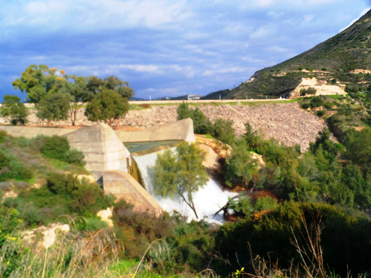 The spillway of the Germasogeia dam with water pouring down between green shrubs and the dam wall behind it
