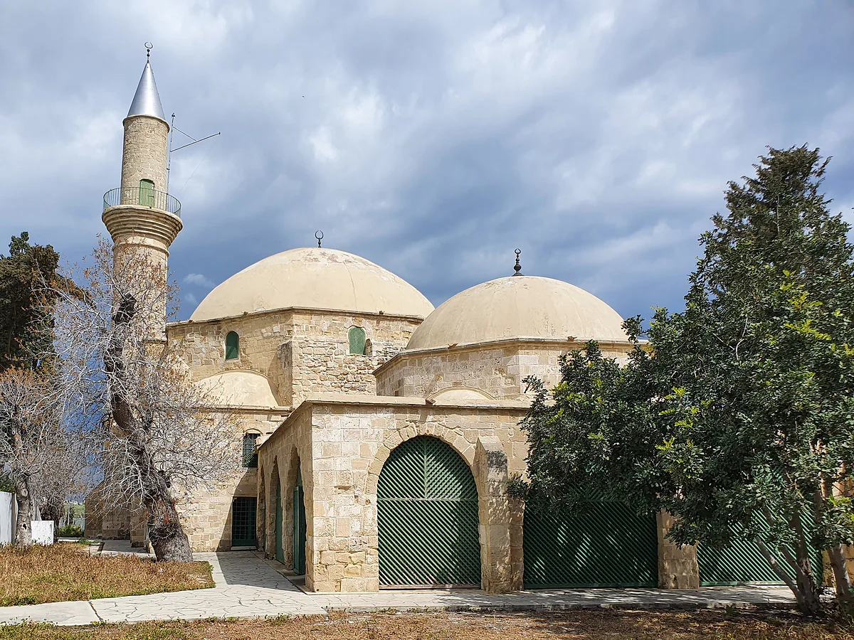 The mosque of Hala Sultan Tekke, in pale stone with low domes, green doors and a slender minaret on the left