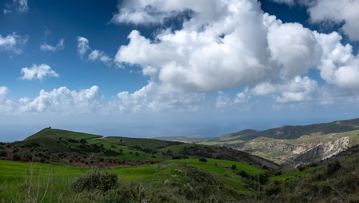 Green hills and ravines running down from the Ineia road towards the Lara coast and the sea, under big white clouds in Akamas
