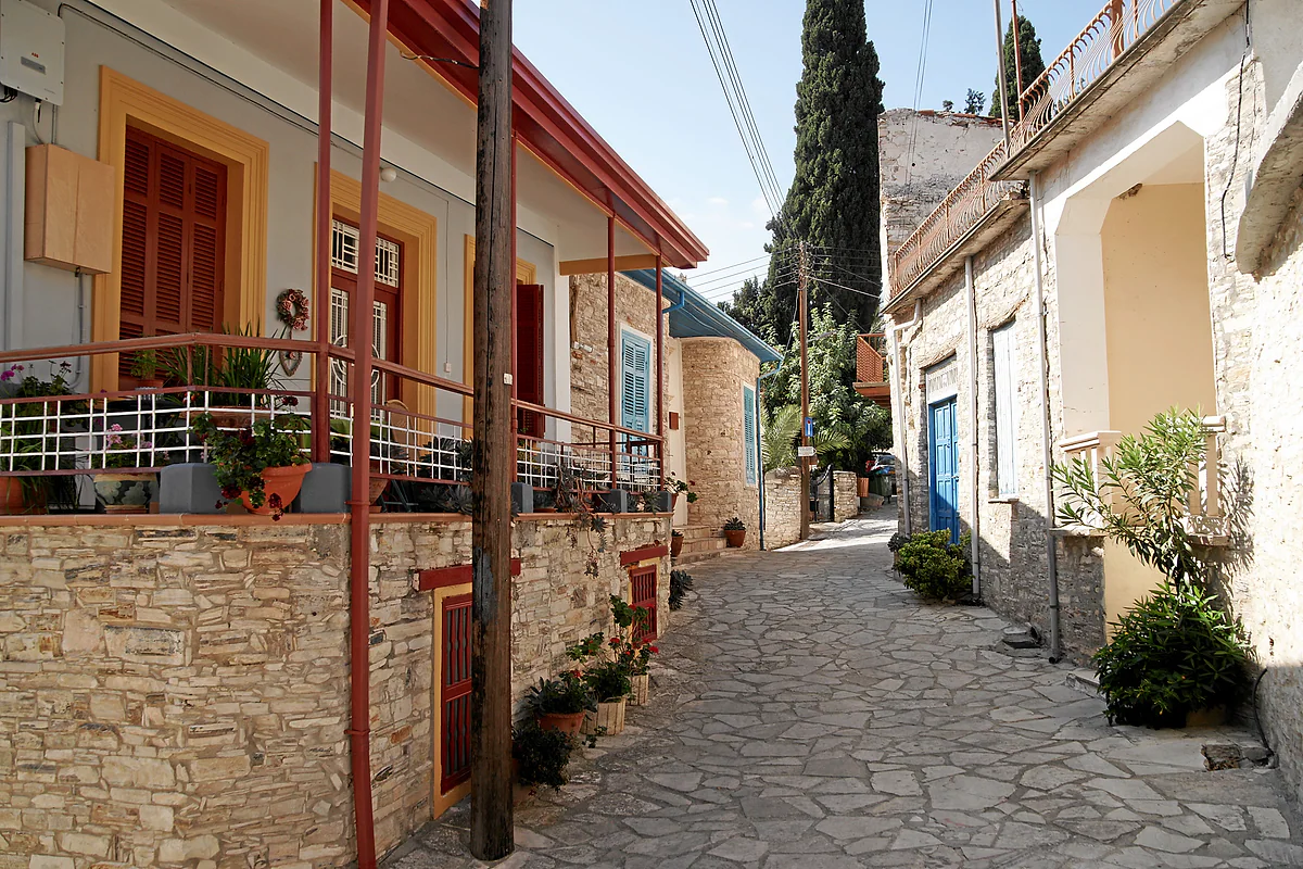 A cobbled lane in Kato Drys between stone houses with colourful wooden balconies and potted plants