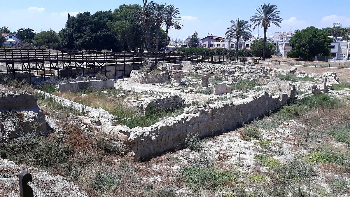 The open-air excavations at Kition, with remains of stone walls among dry grass and a wooden walkway beyond