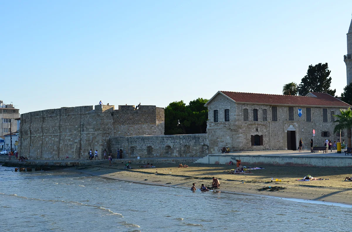 Larnaca fort seen from the shore, with bathers on the sand and a two-storey stone building standing beside it