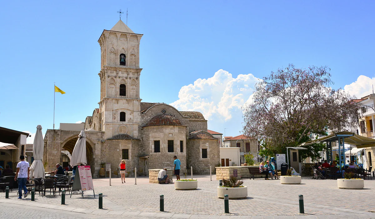 The stone church of Saint Lazarus in Larnaca, with its tall bell tower and domes, seen from the square with café terraces