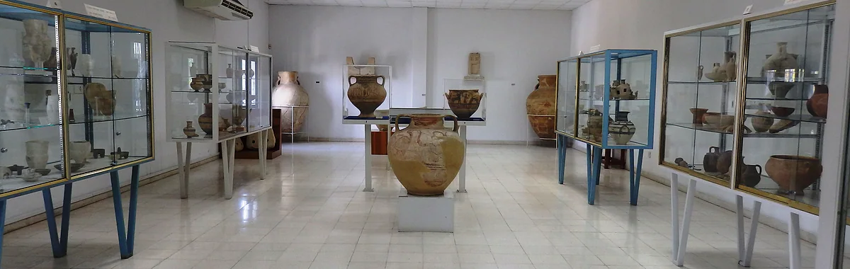 A gallery in the Larnaca Archaeological Museum with display cases of ancient pottery and large clay vessels in the middle