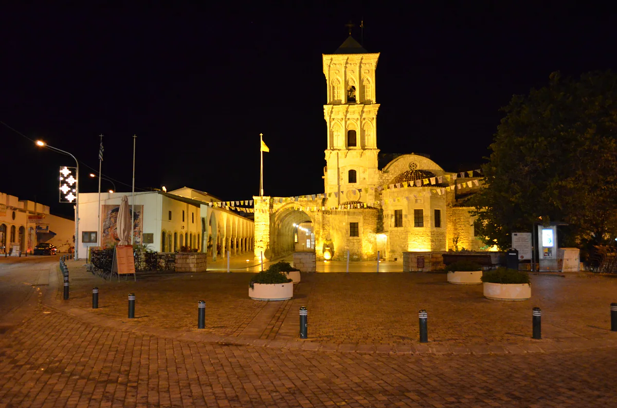 Saint Lazarus church in Larnaca lit up at night, its bell tower glowing gold above the empty paved square in front