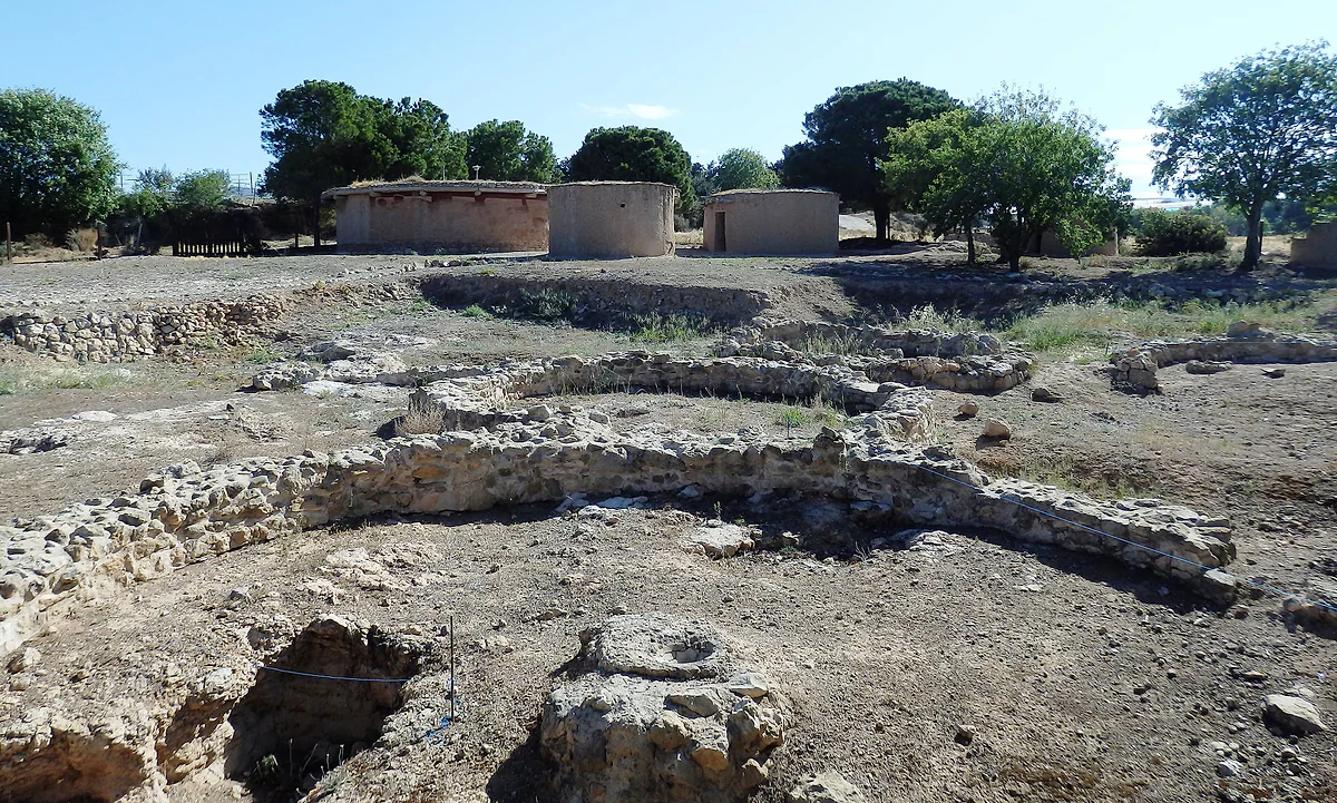 Circular stone foundations of the Chalcolithic settlement at Lempa in the foreground, with three reconstructed round houses behind