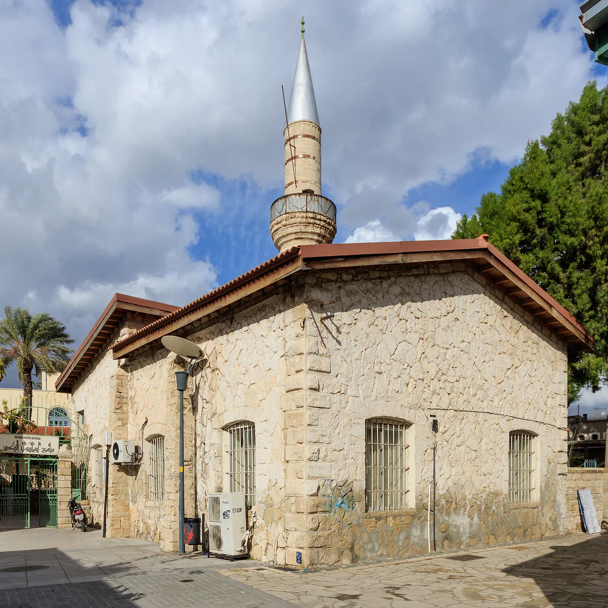The Kebir Mosque in Limassol, built of stone with a tiled roof, and its slender minaret beside the old town trees