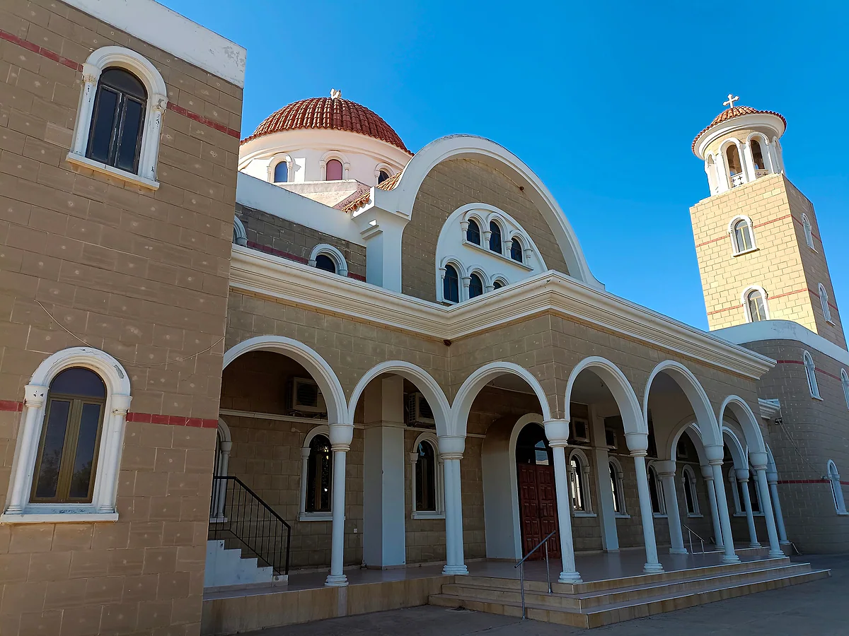 The new church of Panagia Eleousa in Liopetri, with an arched portico, a red dome and a tall bell tower under a blue sky