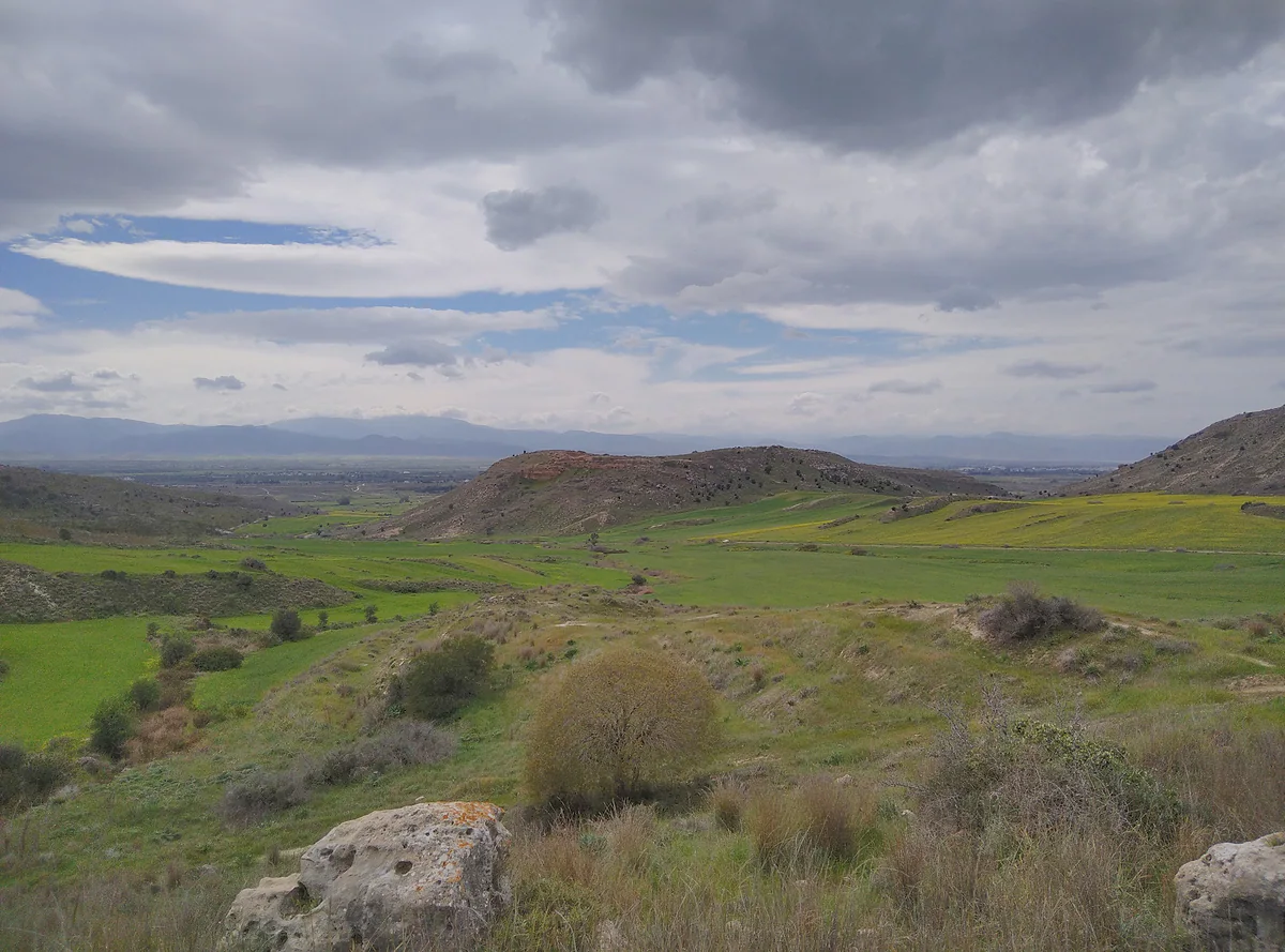 The Morphou plain in spring, with green fields, bare hills and mountains in the distance under a cloudy sky