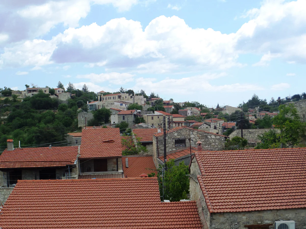 Red tiled roofs and stone houses of Lofou in the foreground, with the rest of the village climbing up the hill behind