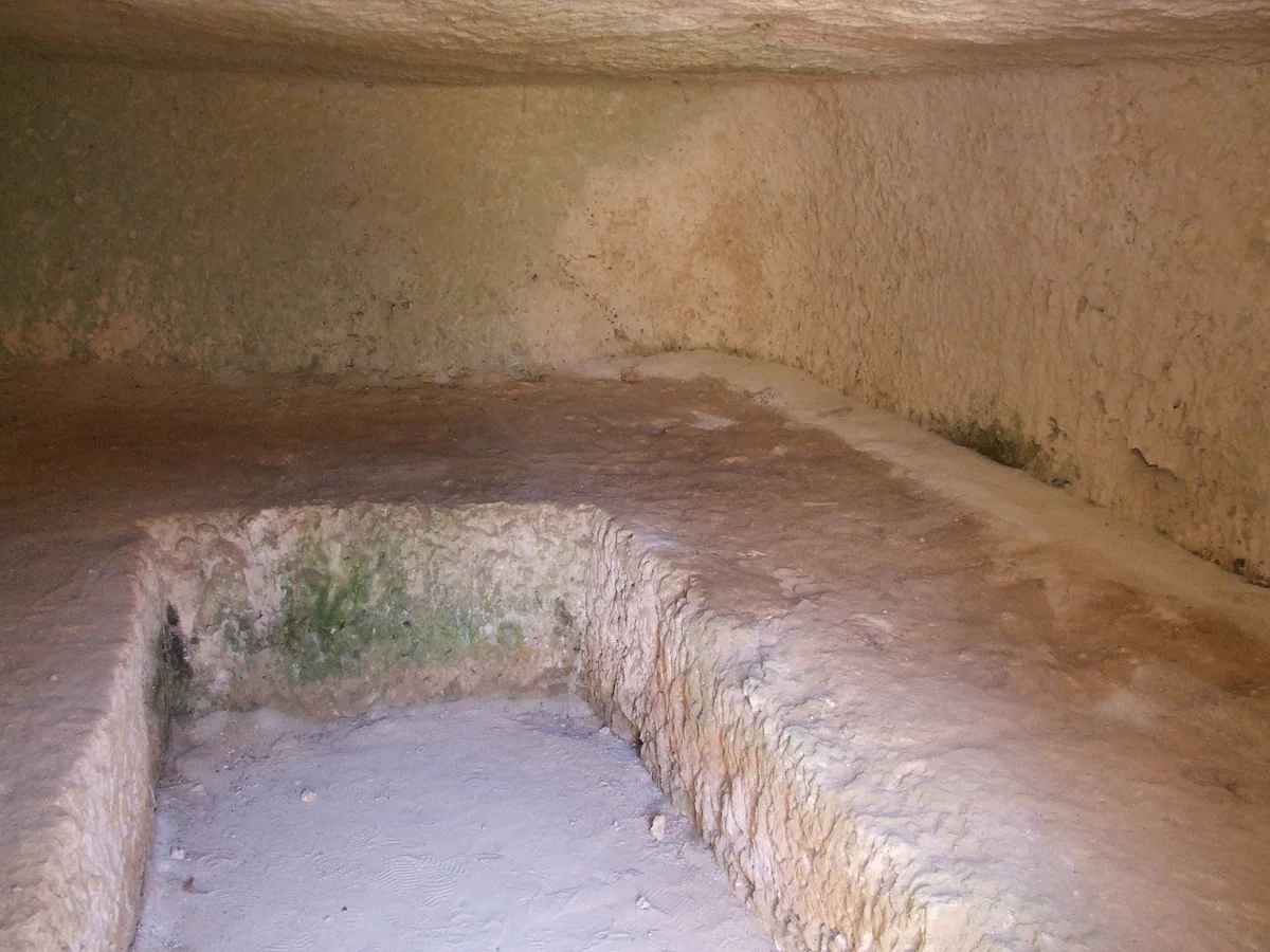 Inside a tomb of the Makronissos necropolis, cut into pale rock, with a carved bench and a burial pit in the floor, near Ayia Napa