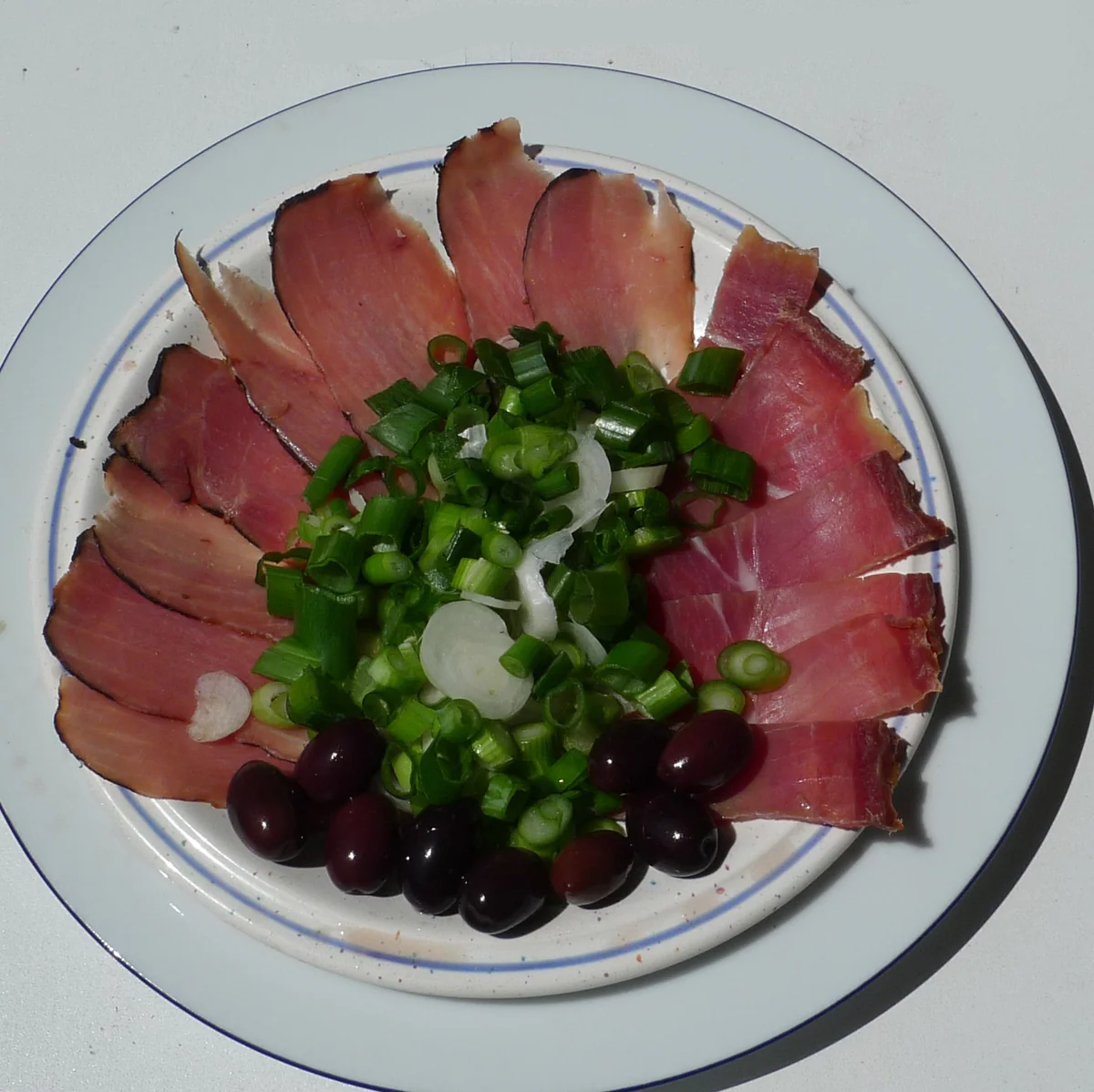 A plate of Cypriot meze with sliced lountza and chiromeri, spring onion, green pepper and black olives