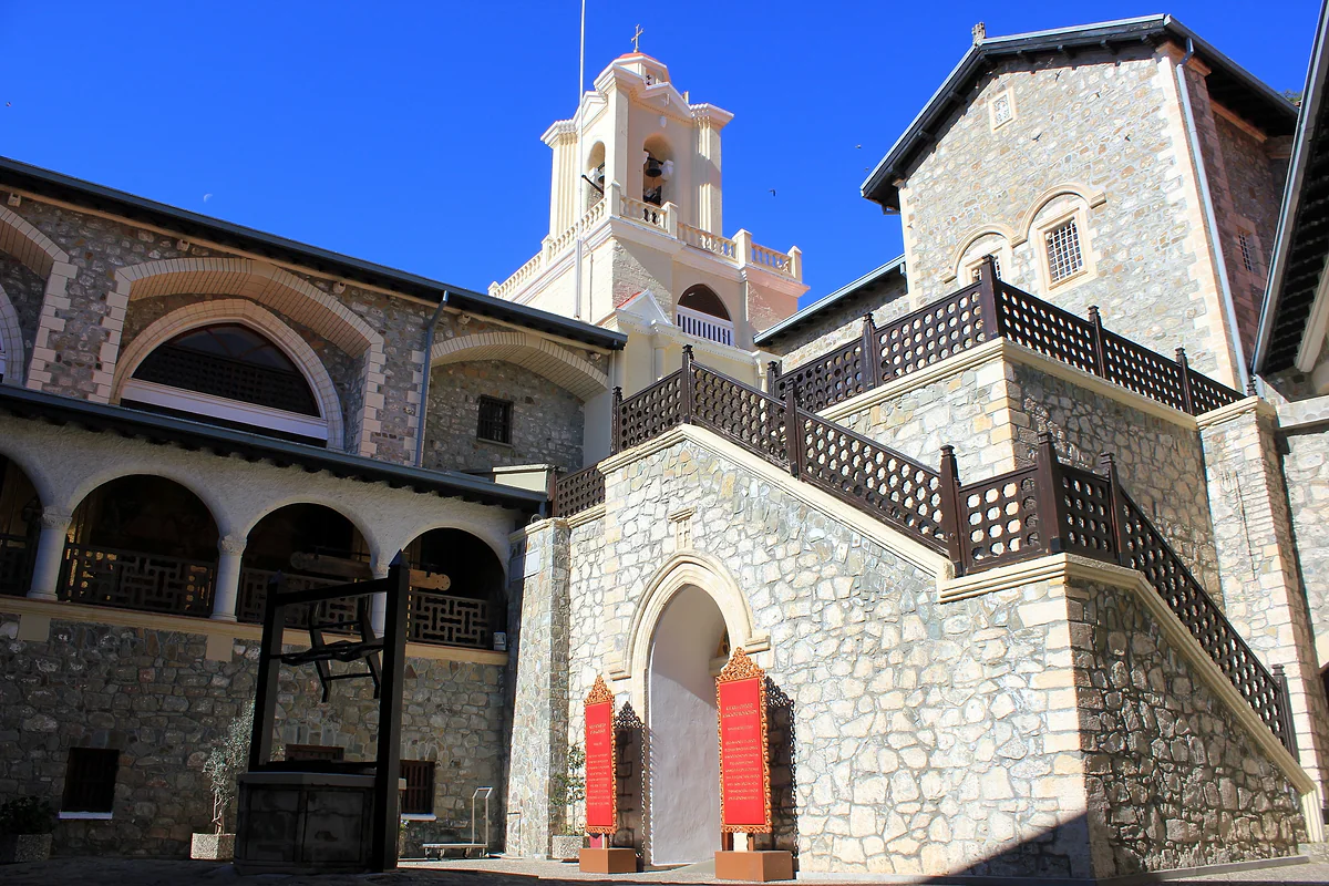 The inner courtyard of Kykkos Monastery, with arcaded galleries, a stone staircase and the bell tower under a deep blue sky