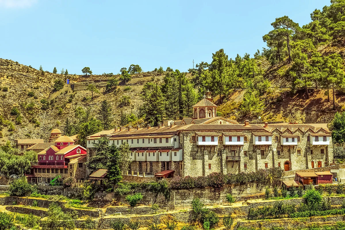 Machairas Monastery above terraces on a pine-covered mountainside under a blue sky