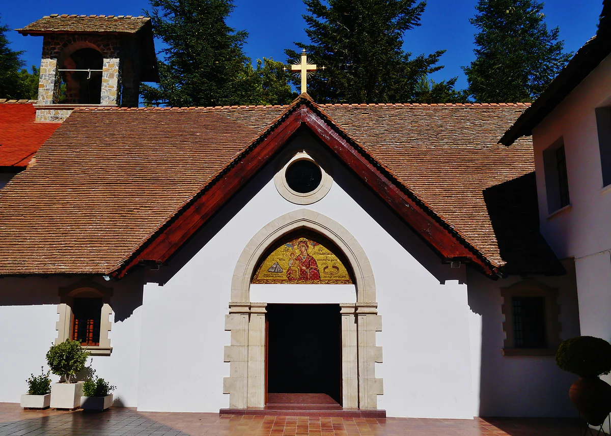 The church of Trooditissa Monastery, with a white façade, an arched doorway with an icon above it and pine trees behind