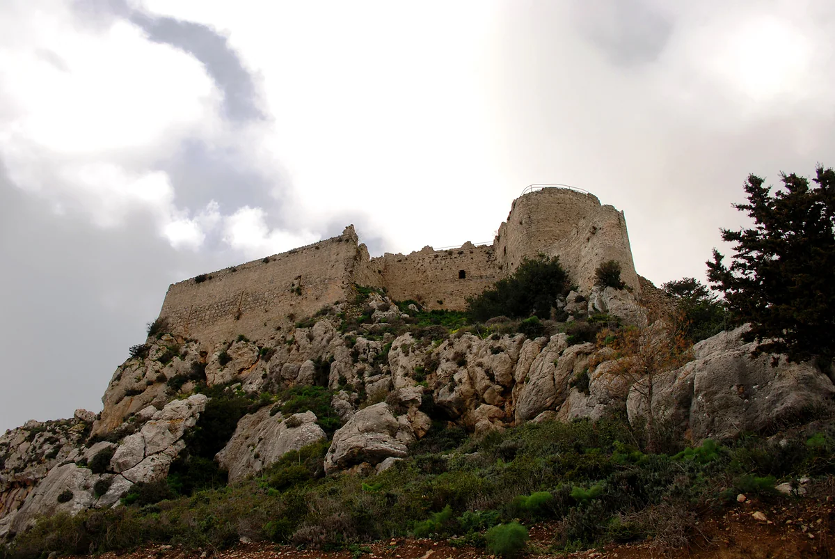 The walls and a round tower of Kantara Castle on the rocks of the Kyrenia range, under a cloudy sky in the north