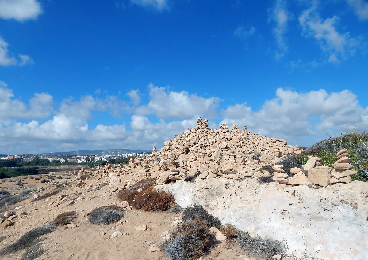 The bare rock and low scrub of the Tombs of the Kings necropolis, with the town of Paphos and its white houses in the distance