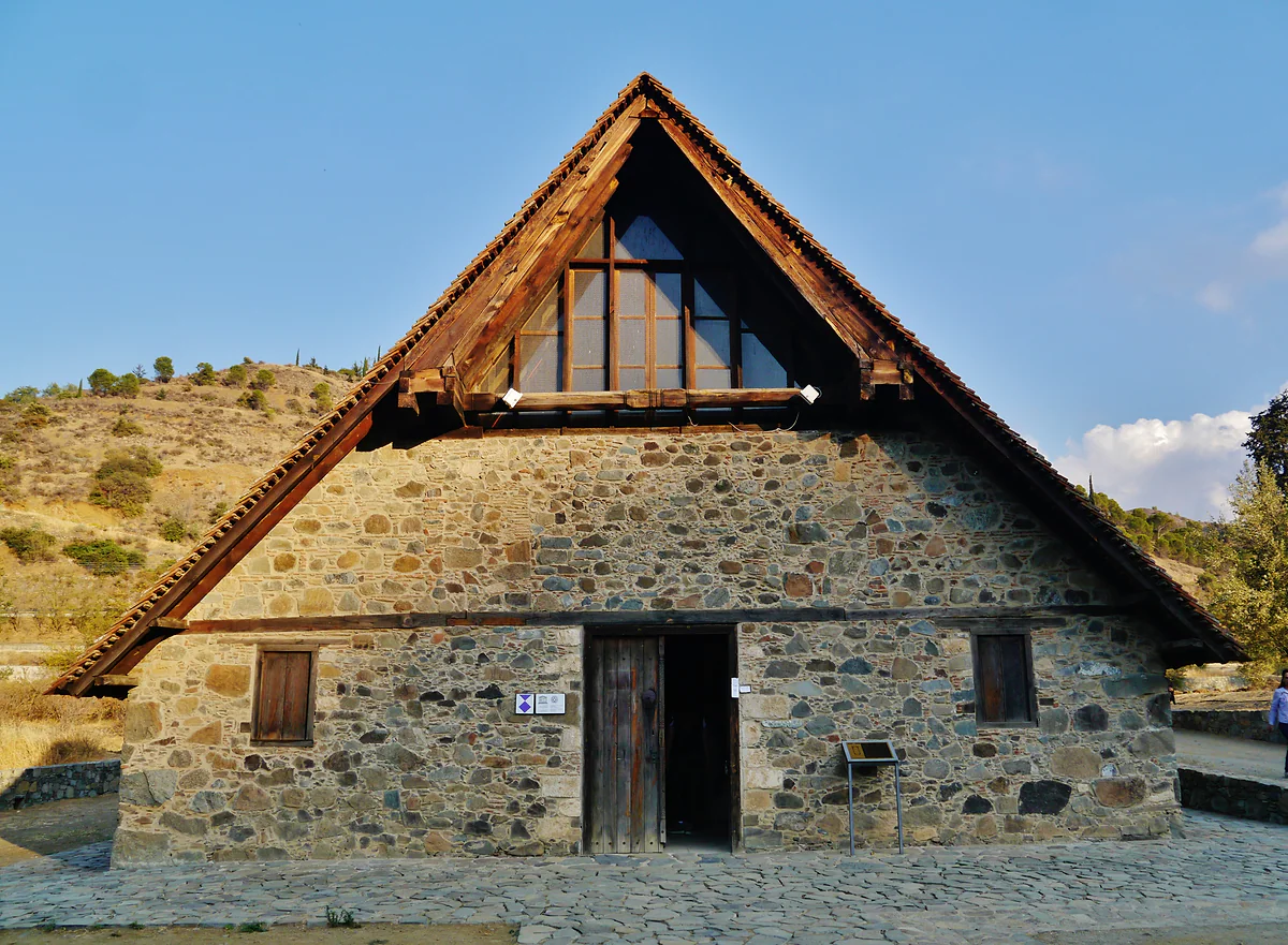 The façade of Panagia Podithou in Galata, a stone church sheltered by a large pitched timber roof that covers it