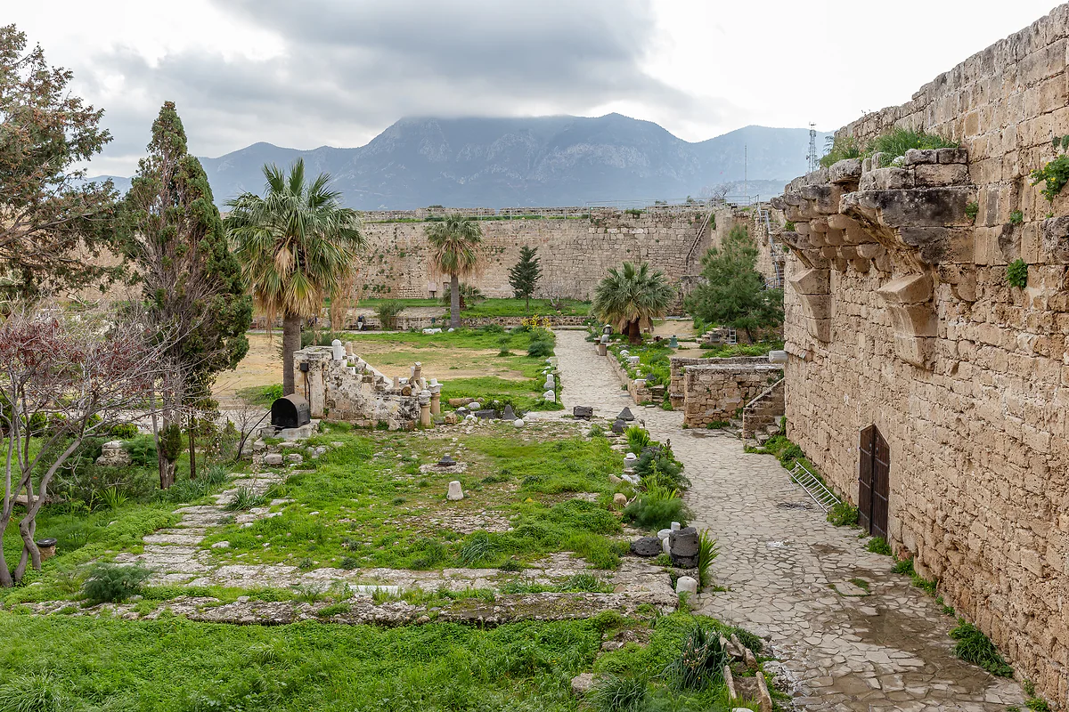 The courtyard of Kyrenia Castle, with lawn, palm trees and stone remains between the walls and the Kyrenia range behind
